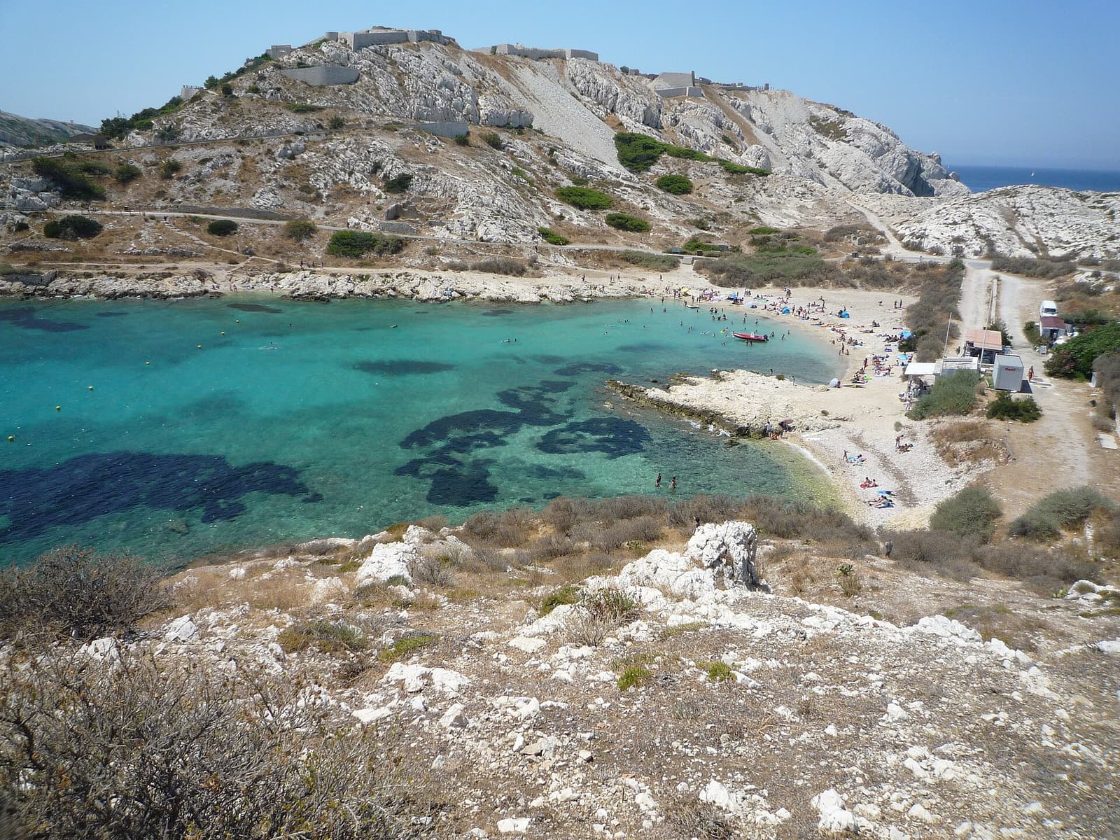 Eine türkisfarbene Bucht mit kleinem Strand unter kahlen weißen Hügeln auf Ratonneau, Frioul-Inseln