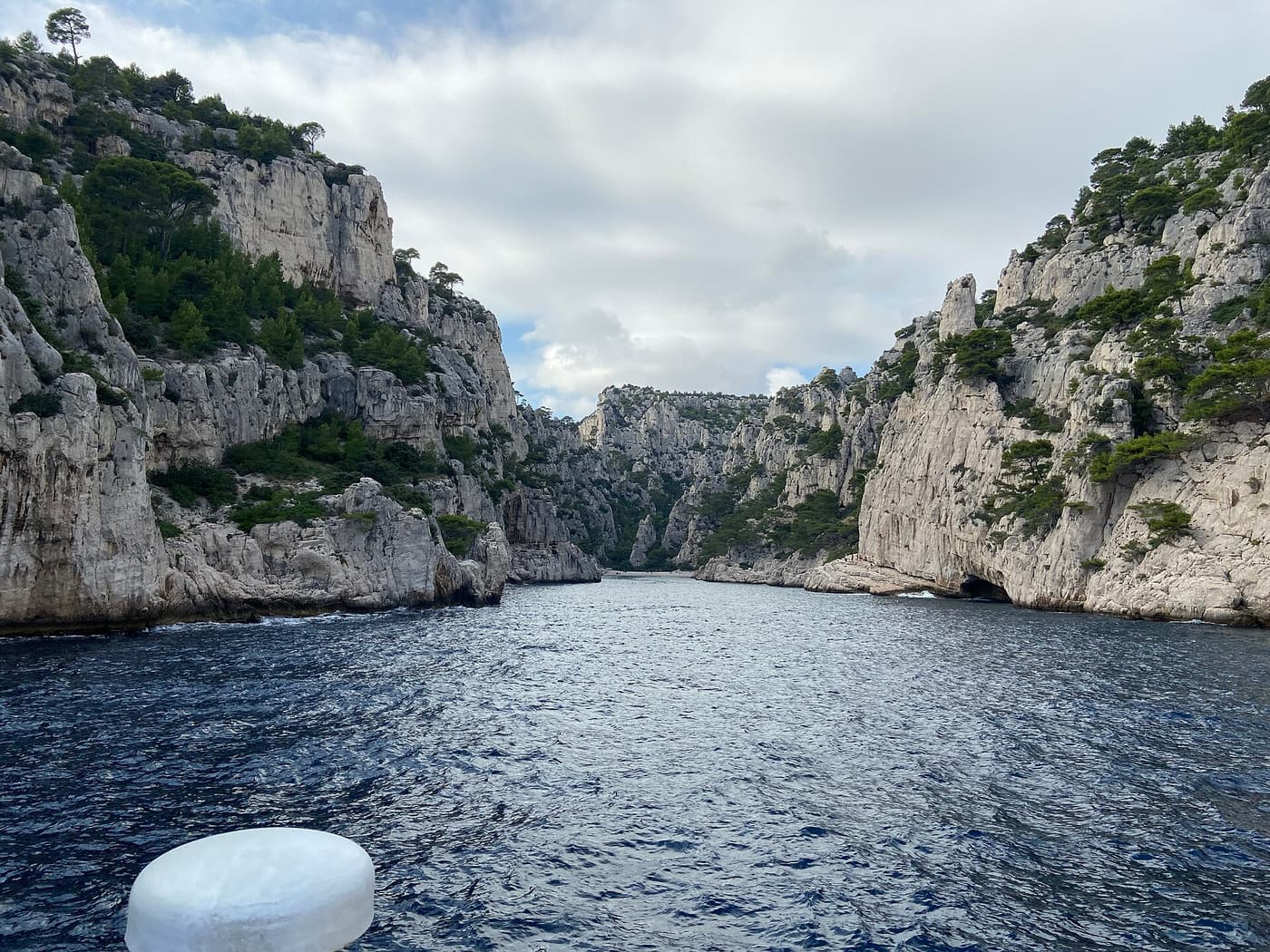 A small boat anchored in the turquoise water of the Calanque d'En-Vau below vertical cliffs