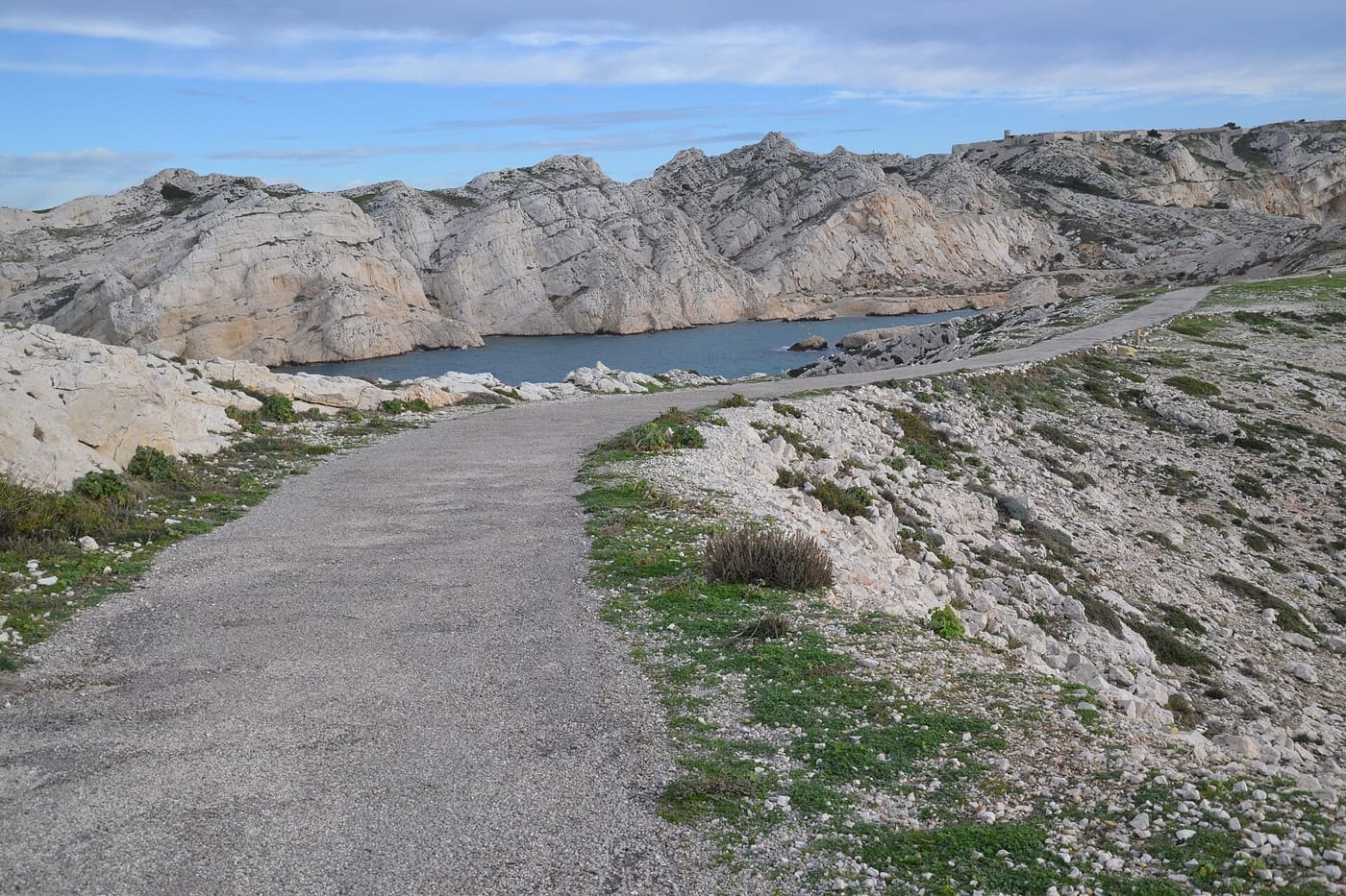 A rocky footpath on the Frioul islands leading towards a cove of clear water