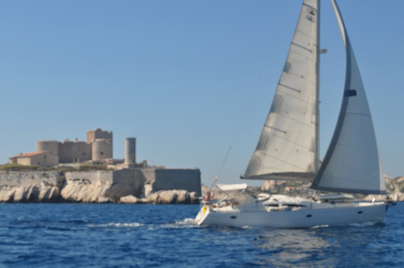 Eine weiße Segeljacht fährt an einem hellen Tag am Château d’If vorbei
