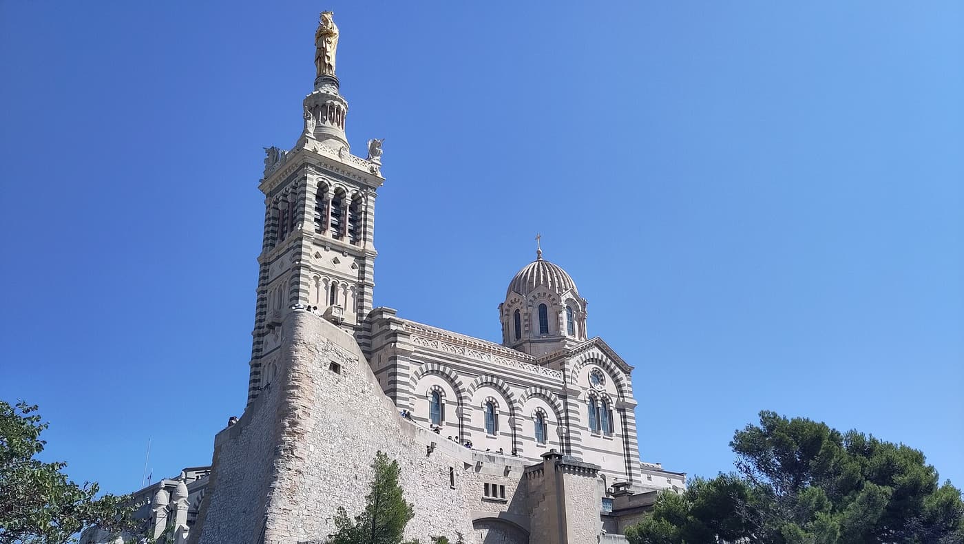 The basilica of Notre-Dame de la Garde with its bell tower and golden statue against a blue sky