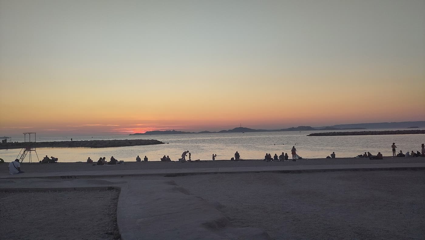 People on the Prado beach in Marseille watching the sun set over the sea